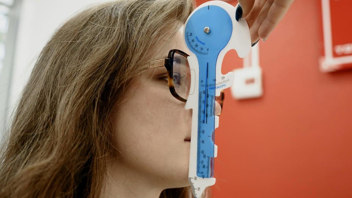 Optometrist using a blue measurement tool for vision assessment on a young female patient.