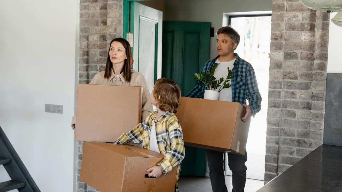 Family entering a new house, carrying boxes and a plant, symbolizing a fresh start.