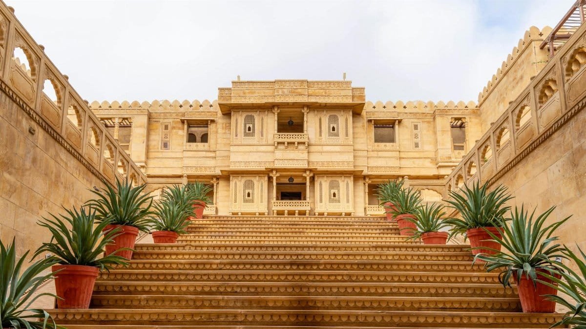 Stunning sandstone palace entrance in Jaisalmer, Rajasthan, India, with ornate steps and potted plants.