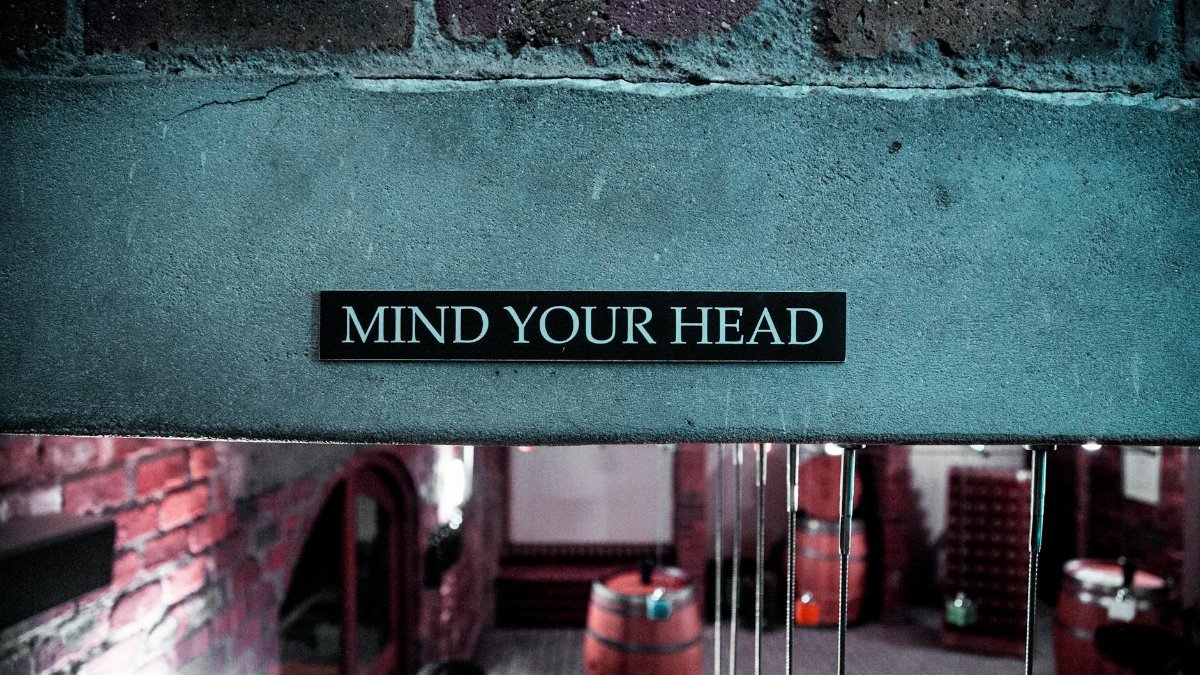 A 'Mind Your Head' sign in a rustic brick barrel cellar setting, creating a safety awareness ambiance.