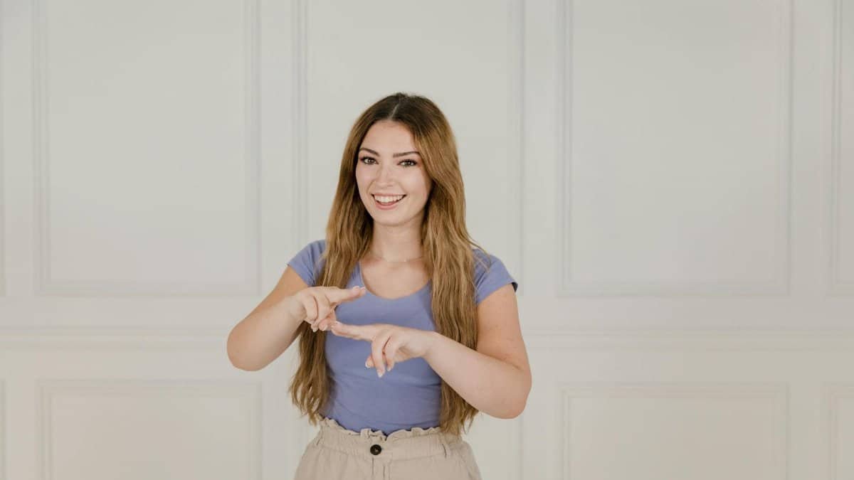Smiling woman with long hair gestures in sign language against a white background.