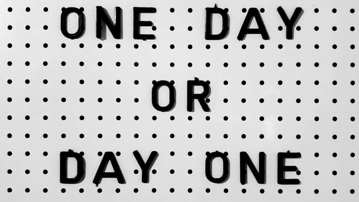 Black letters on white board saying 'One Day or Day One?' with polka dot design.