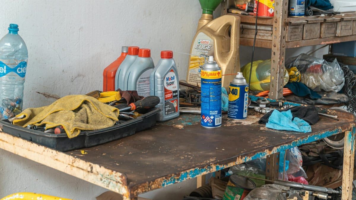 A cluttered workbench in an automobile garage with tools, oil cans, and maintenance products.