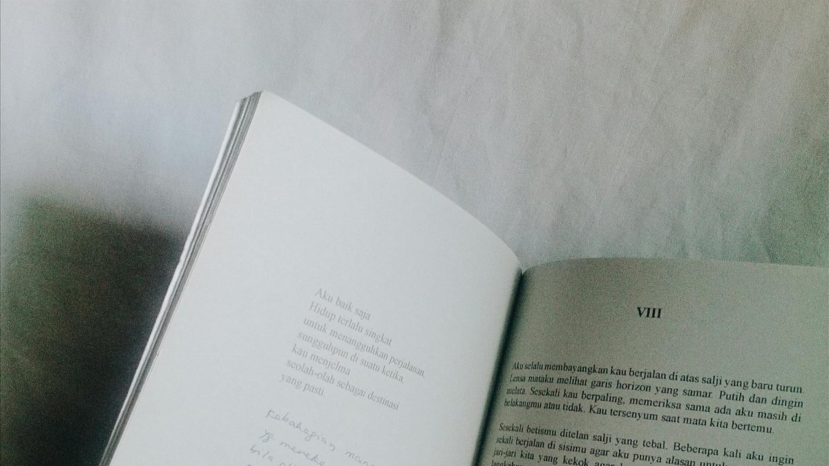 Open book with text on white surface, minimalist and monochrome style.