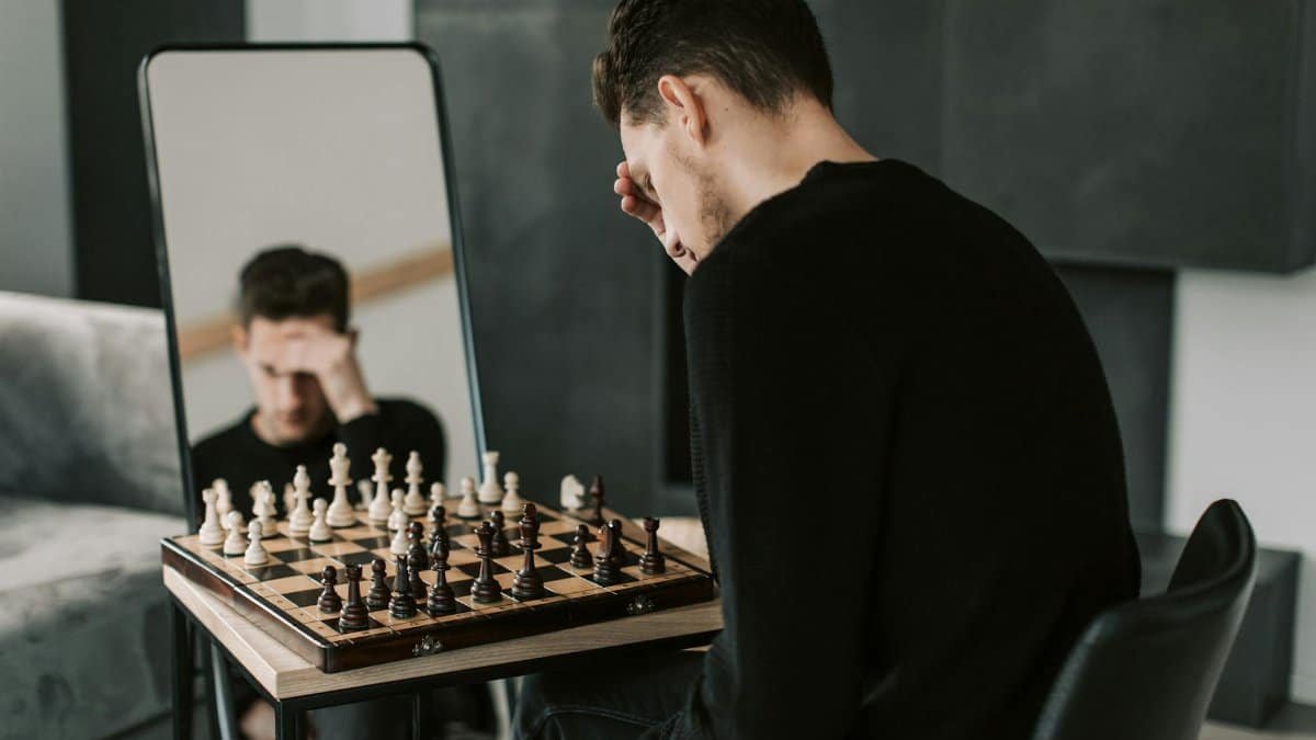 Man deeply engrossed in a chess game, reflected in a mirror, indoors.