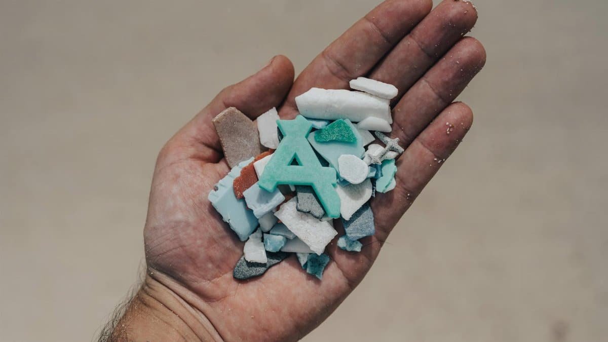 Close-up of a hand holding colorful plastic fragments, highlighting environmental concerns.