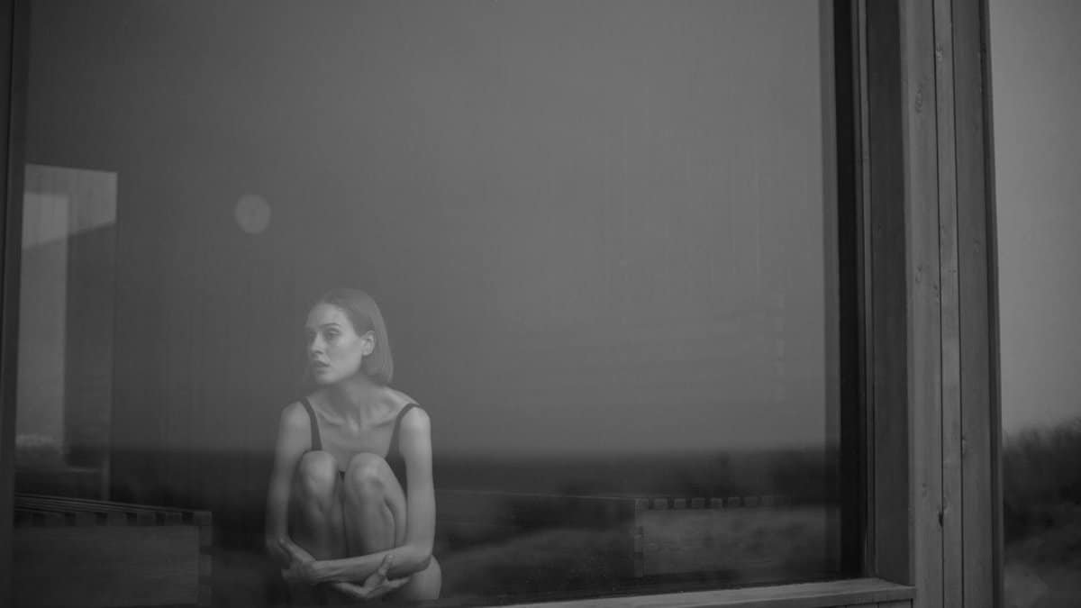 A woman sitting near a window in grayscale, evoking solitude and reflection.