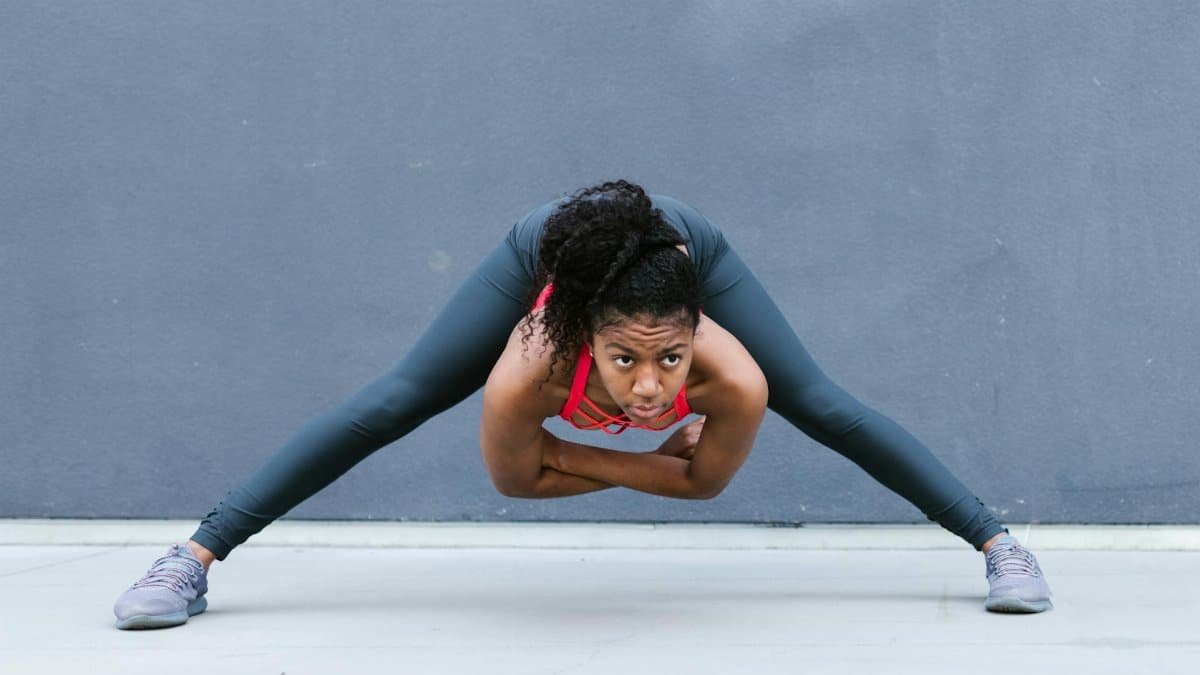 African American woman in activewear performing a stretch outdoors, showcasing strength and determination.