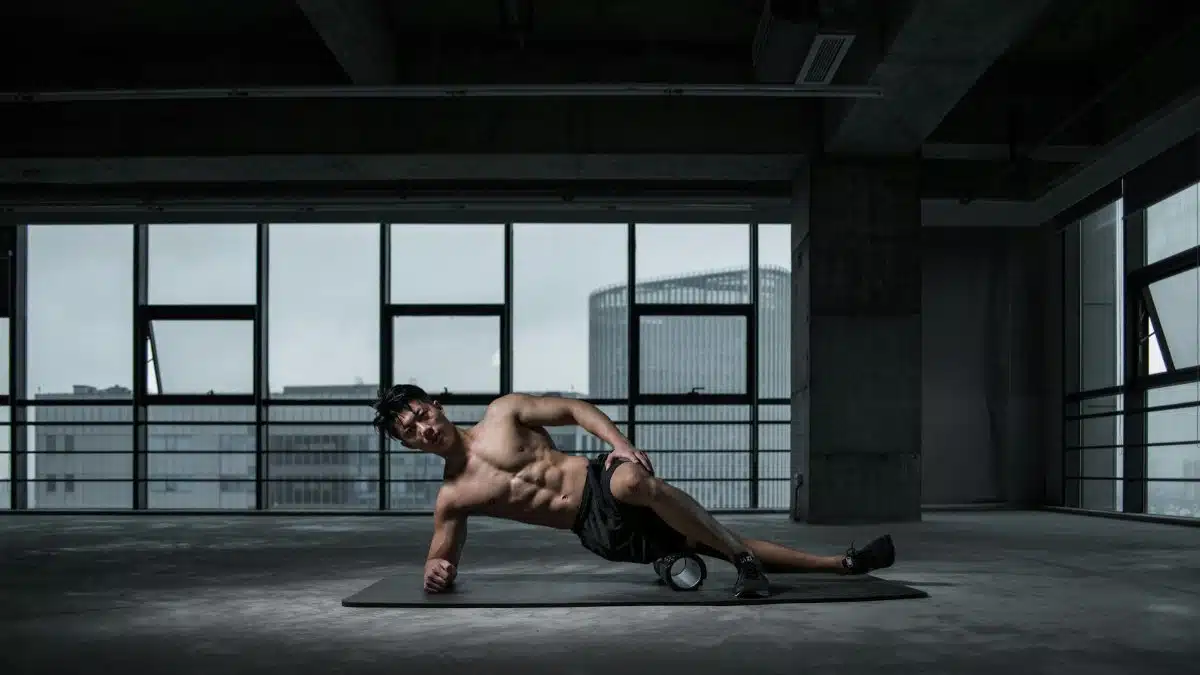 Muscular man performing yoga stretch indoors on a mat with urban window view in the background.