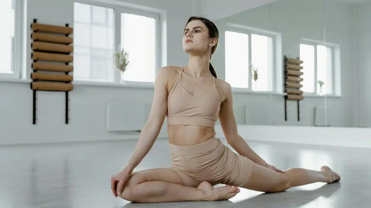 A young woman practices yoga in a bright, minimal studio setting, demonstrating a pigeon pose.
