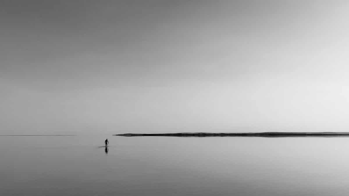 A lone figure stands in tranquil waters beneath a vast, serene sky, embodying solitude and reflection.