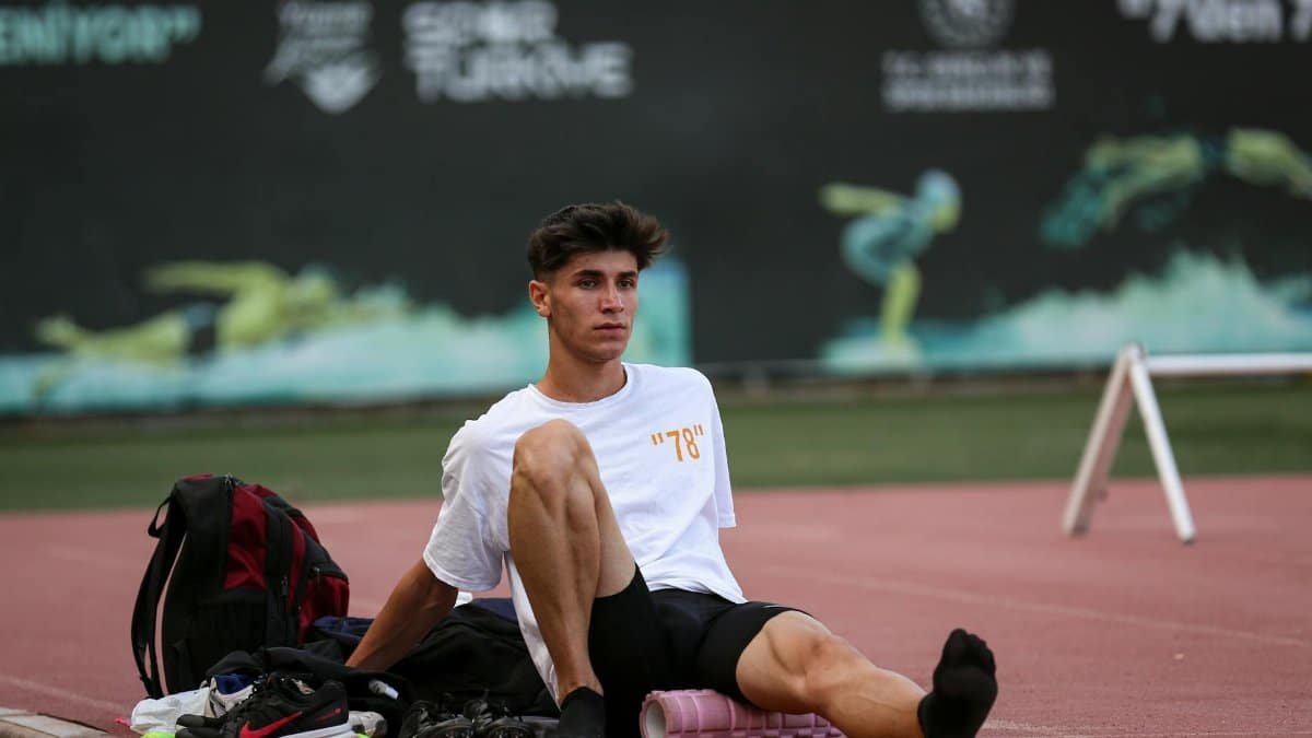 Athlete in sportswear using a foam roller on a track, preparing for training.
