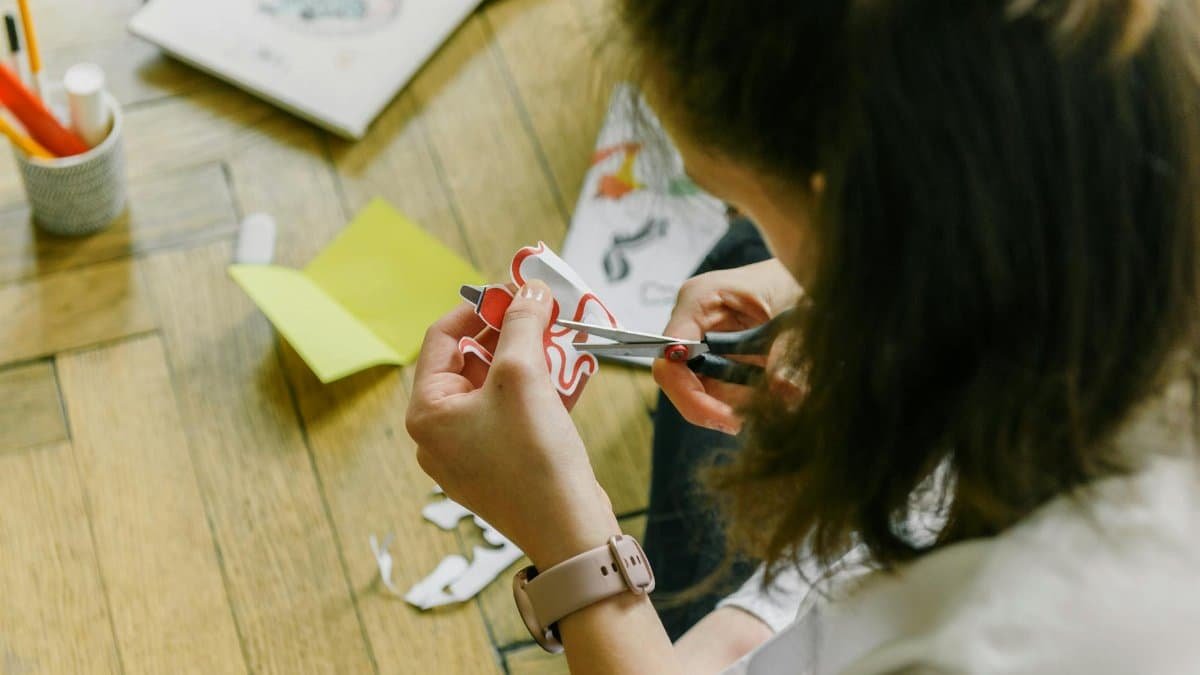 Creative woman using scissors to cut paper designs at home.