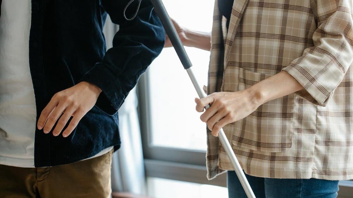 Individuals in casual attire offering support with a walking stick indoors.