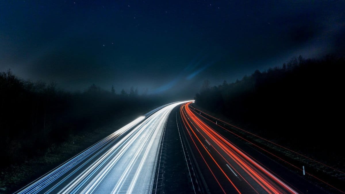Long exposure night shot capturing stunning red and white light trails on a highway under a starry sky.