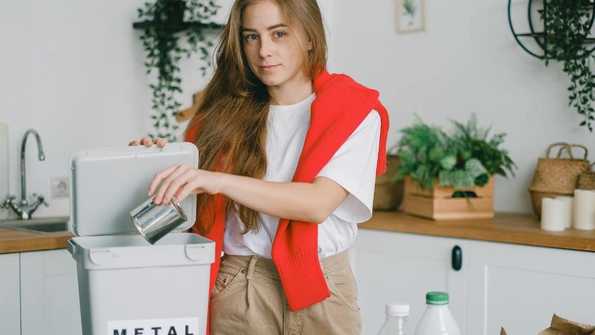 Responsible female sorting garbage while putting tin can into container for metal litter and looking at camera