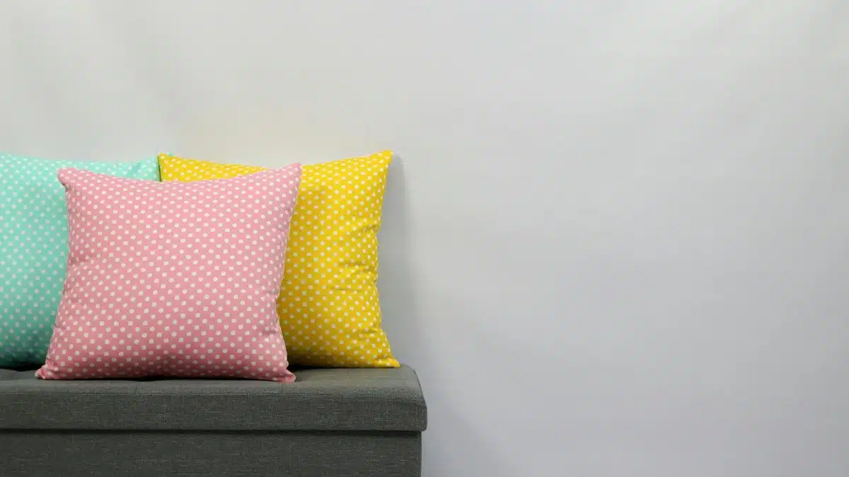 Three vibrant polka dot pillows on a grey sofa with a minimalistic background.