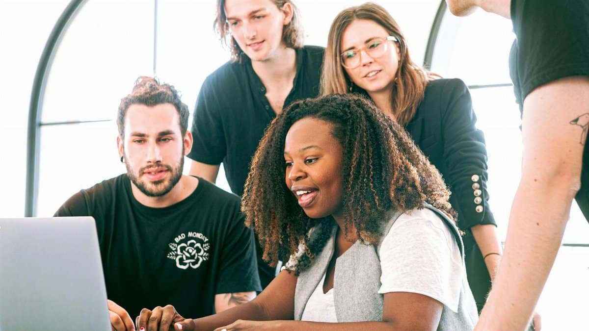 A diverse group of young professionals collaborating around a laptop in a modern office setting. Perfect for business or tech concepts.