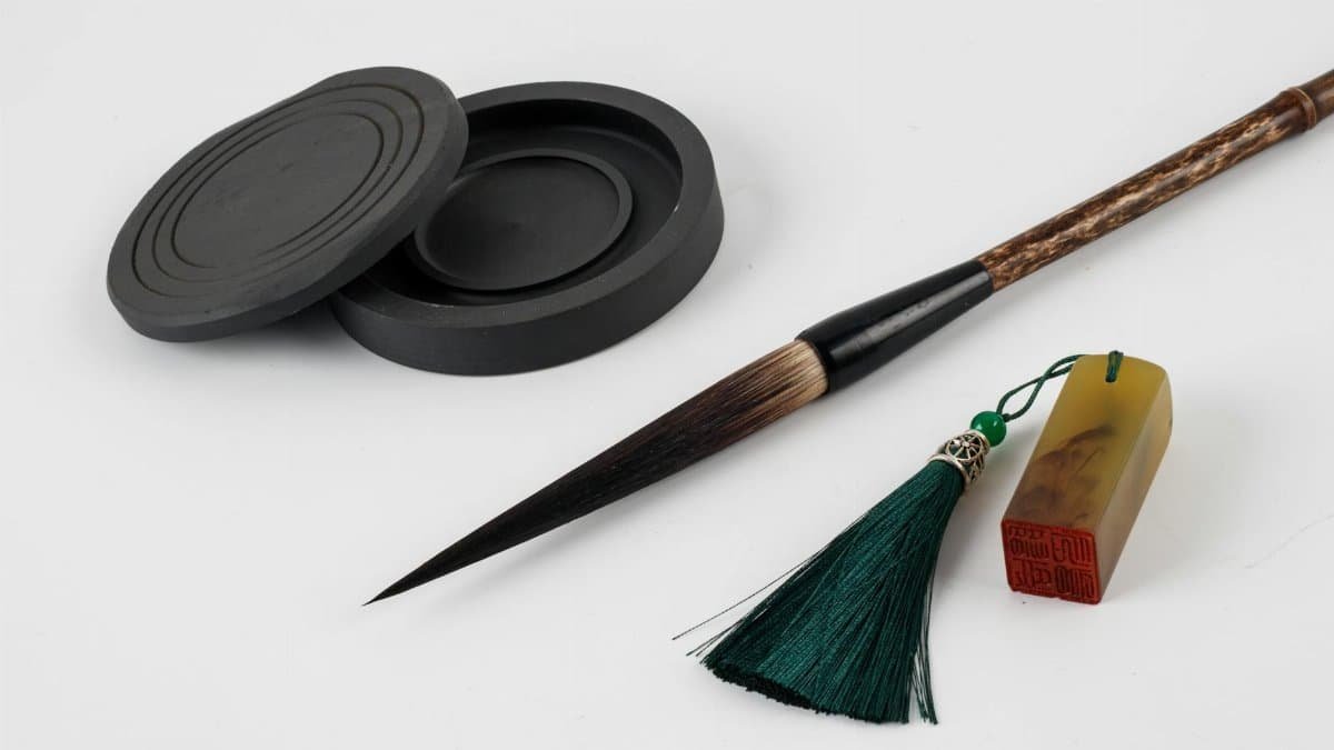 Close-up of traditional Asian calligraphy tools including ink stone, brush, and seal on white background.