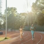 Two women jogging on an outdoor track, enjoying exercise and fitness in the morning sun.