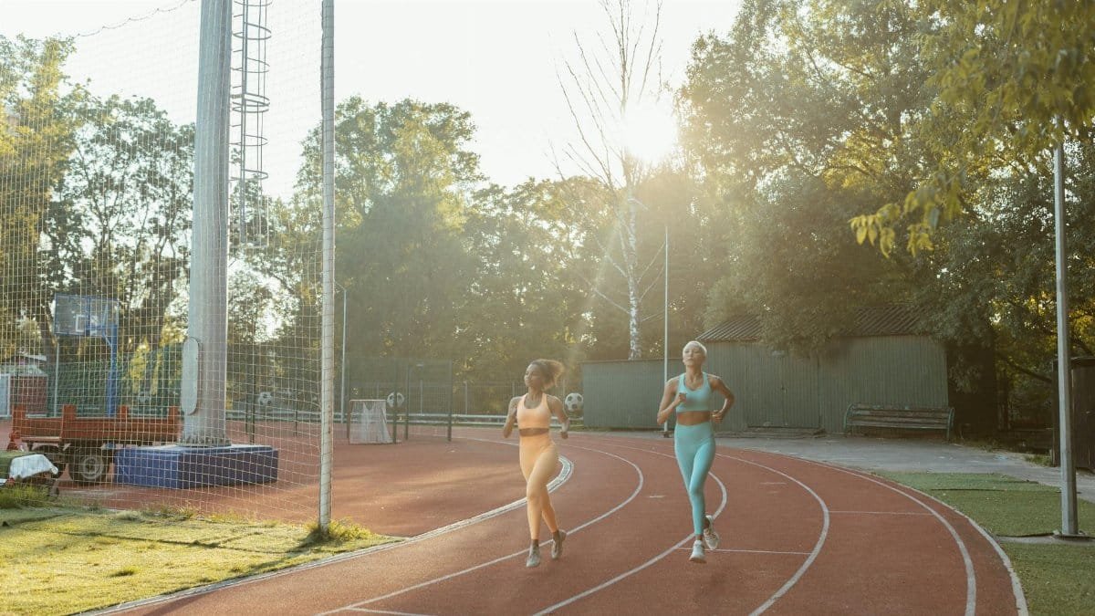 Two women jogging on an outdoor track, enjoying exercise and fitness in the morning sun.