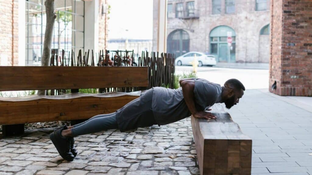 Fit man doing push-ups on a bench in an urban outdoor setting, focusing on fitness and healthy lifestyle.