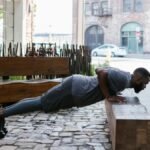 Fit man doing push-ups on a bench in an urban outdoor setting, focusing on fitness and healthy lifestyle.
