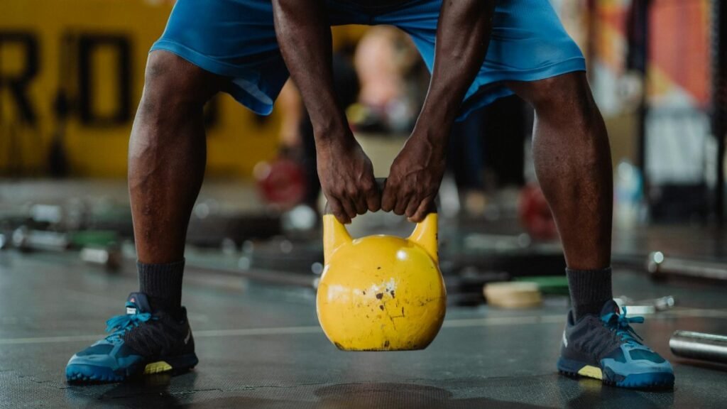 Focused workout scene of athlete lifting a yellow kettlebell in the gym.