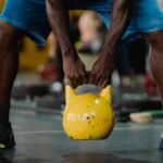 Focused workout scene of athlete lifting a yellow kettlebell in the gym.