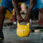 Focused workout scene of athlete lifting a yellow kettlebell in the gym.