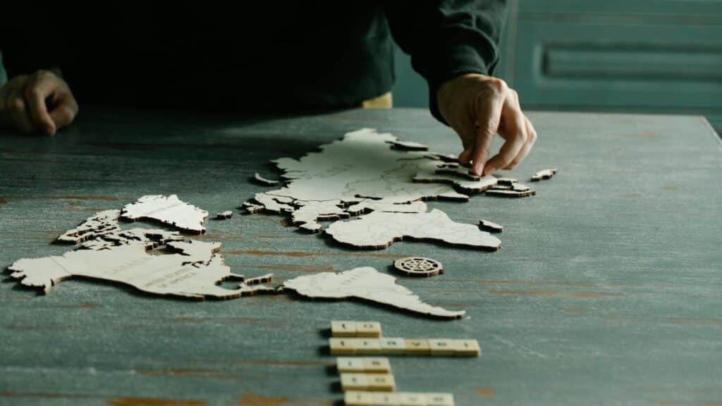 A person arranging a wooden puzzle of a world map on a rustic wooden table.
