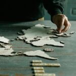 A person arranging a wooden puzzle of a world map on a rustic wooden table.