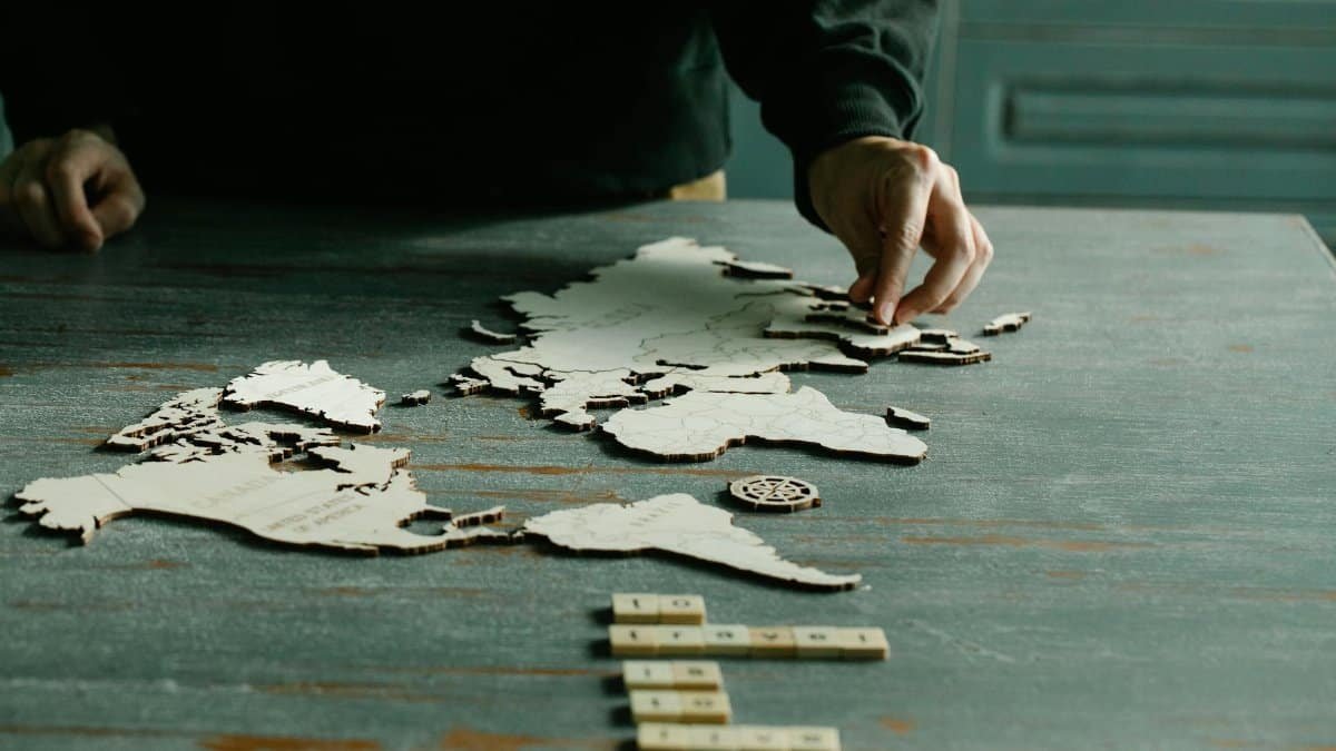 A person arranging a wooden puzzle of a world map on a rustic wooden table.