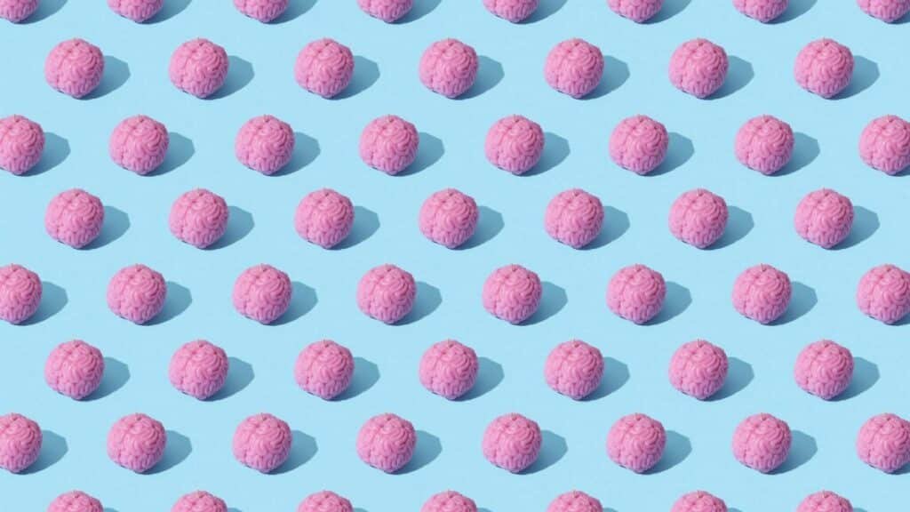 Creative composition of pink brain models in a repeating pattern on a light blue surface, showcasing abstract thinking.