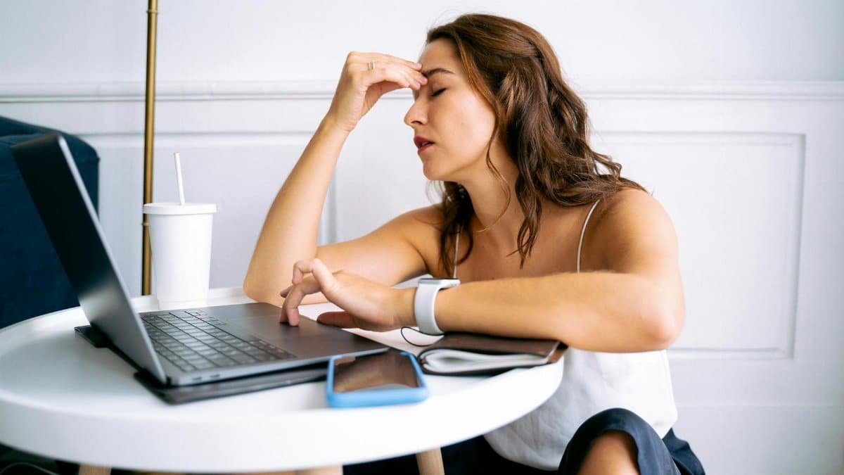 Woman experiencing work fatigue with laptop at a table, indicating stress and tiredness.