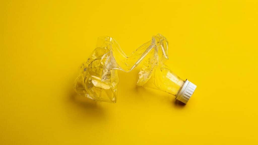 A crumpled plastic bottle against a bright yellow backdrop, highlighting recycling themes.