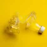 A crumpled plastic bottle against a bright yellow backdrop, highlighting recycling themes.