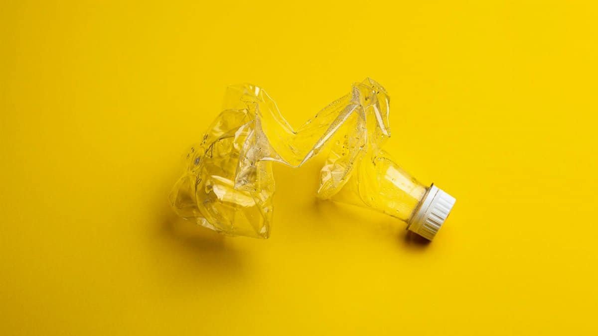 A crumpled plastic bottle against a bright yellow backdrop, highlighting recycling themes.