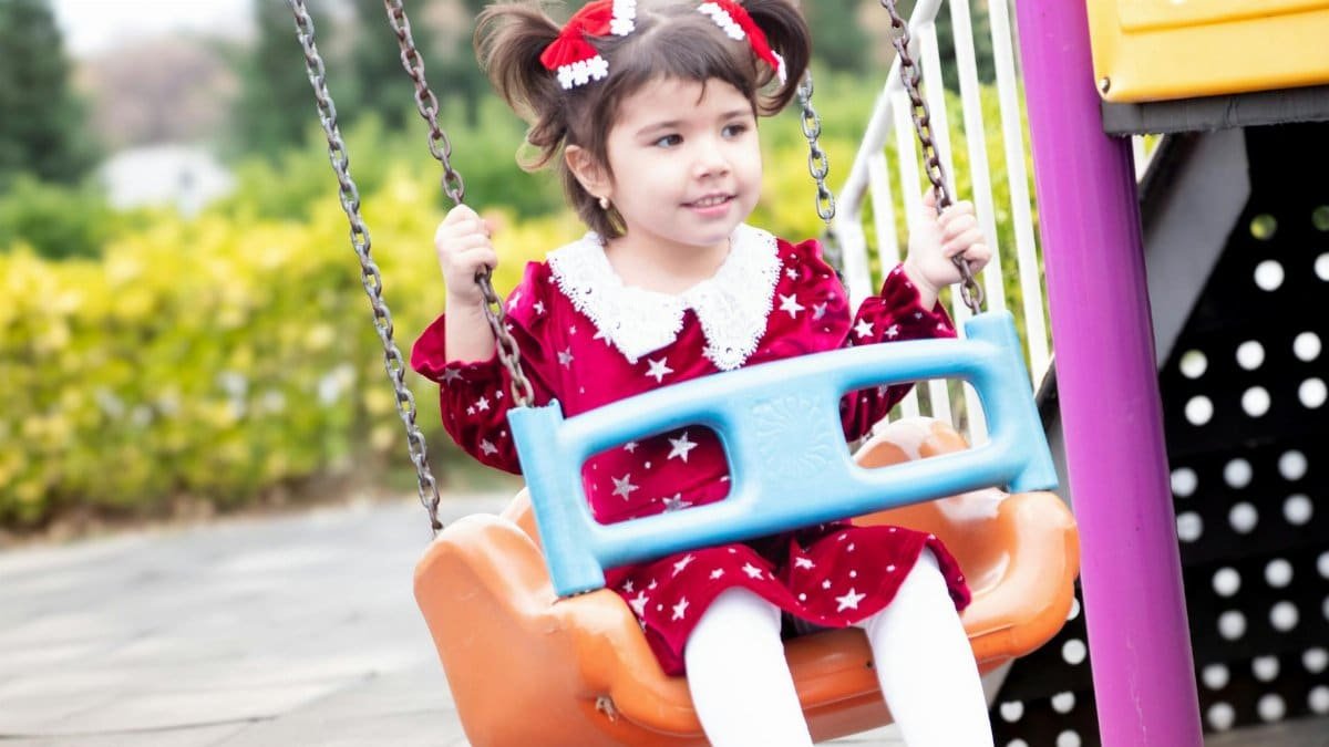 A joyful child in red dress on a swing in Salyan, Azerbaycan park.
