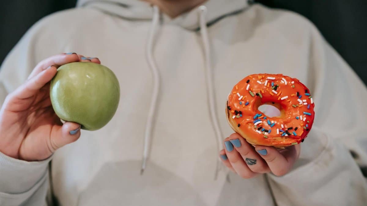 A person holding both an apple and a donut, symbolizing a food choice dilemma.