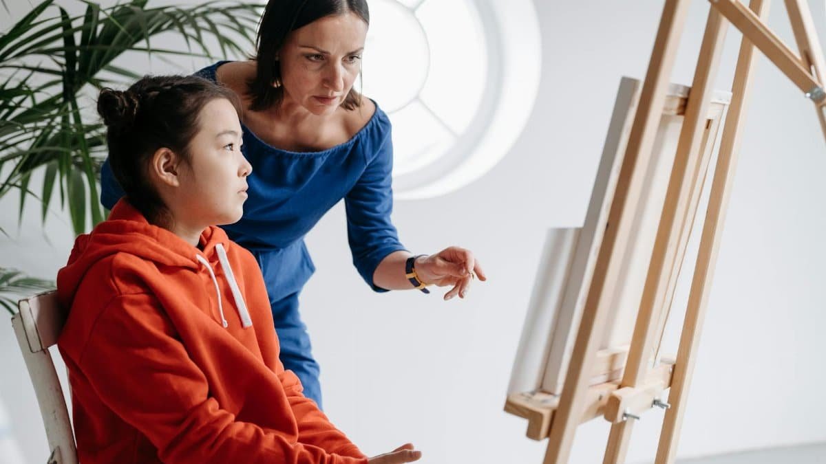 Young student learning painting with guidance from a teacher in a bright art studio.