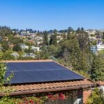 Solar panels on a suburban home, surrounded by lush greenery and a sunny blue sky.