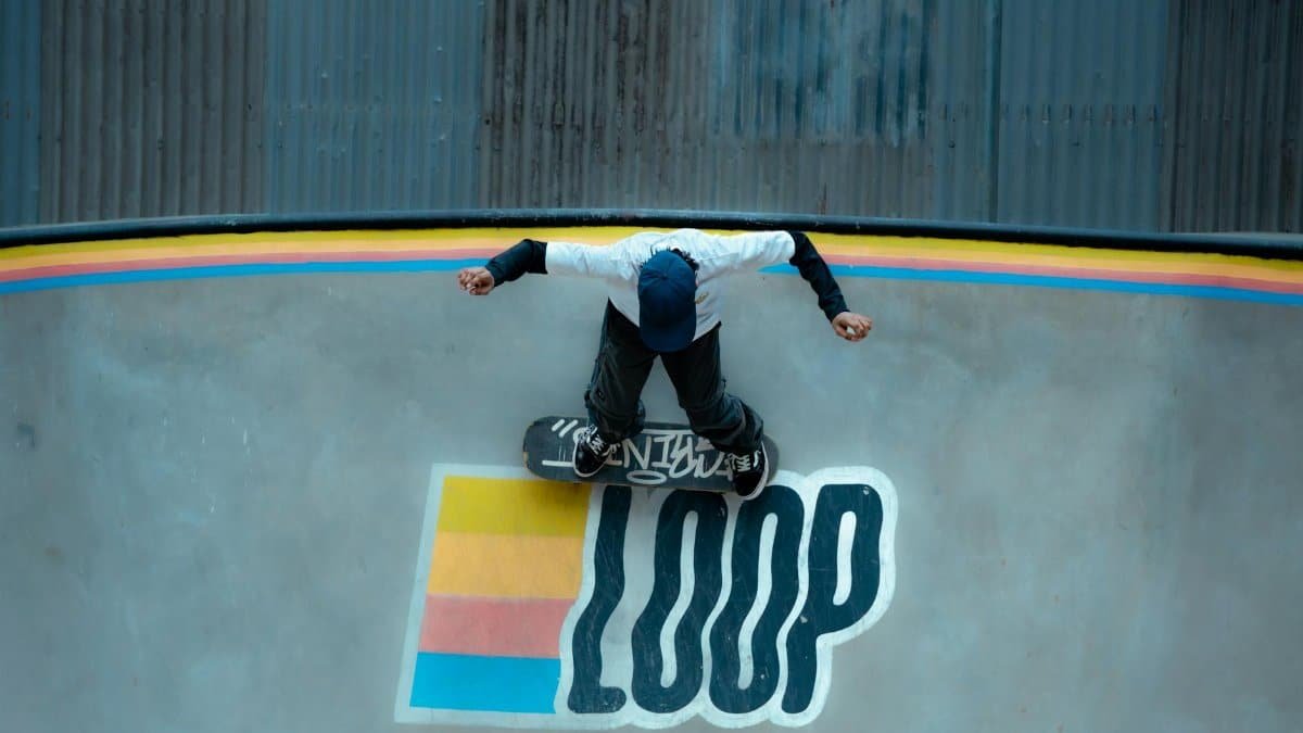 A skateboarder performs a trick on a colorful loop ramp from an aerial view.