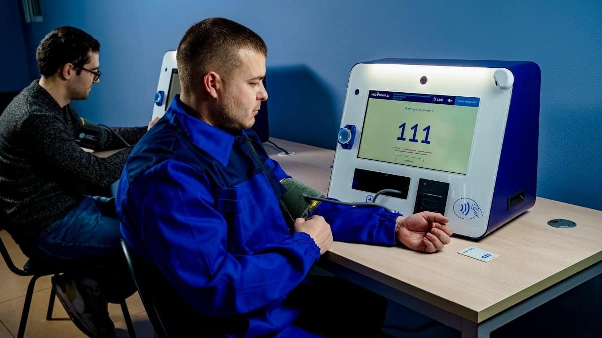 Two men using a blood pressure machine at a clinic, focusing on health monitoring with modern devices.