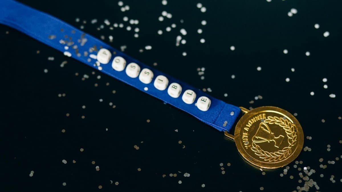 Close-up of a gold medal on a blue ribbon with 'possible' beading, symbolizing achievement.