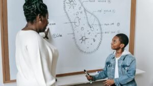 A teacher and student engage in a biology lesson with a cell diagram on the whiteboard.