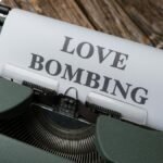 Close-up of a vintage typewriter printing 'Love Bombing' on paper, placed on a wooden desk.