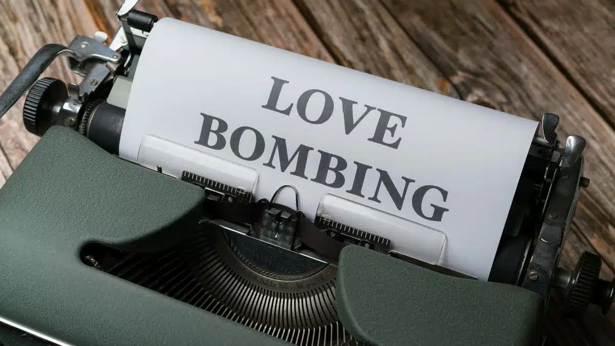 Close-up of a vintage typewriter printing 'Love Bombing' on paper, placed on a wooden desk.