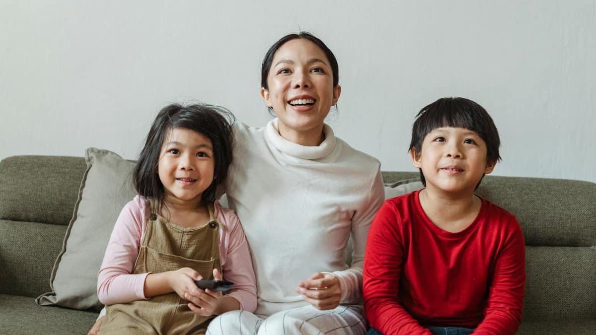 Mother and children enjoying a movie at home, smiling and relaxed on the sofa.