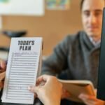 Two colleagues organizing tasks with a plan and sticky notes during a team meeting.